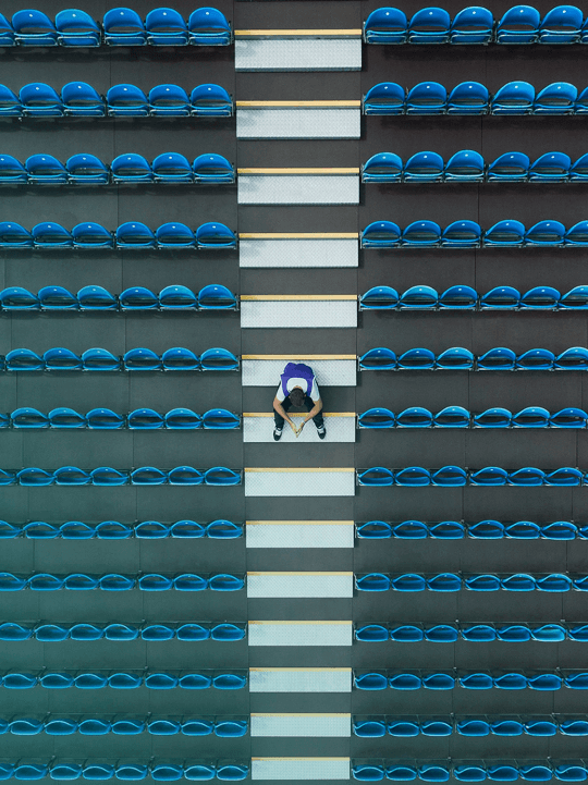 An overhead photograph of a man sat on some stairs between rows of seats